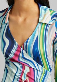 Bunte Bluse mit Kragen, verziert mit wirbelnden Mustern in Blau, Grün und Pink, gefertigt aus glattem Stoff mit figurbetontem Schnitt.