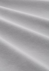 Tela de algodón blanca con una textura suave, que presenta líneas diagonales sutiles y pliegues, mostrando la elasticidad y suavidad del material.