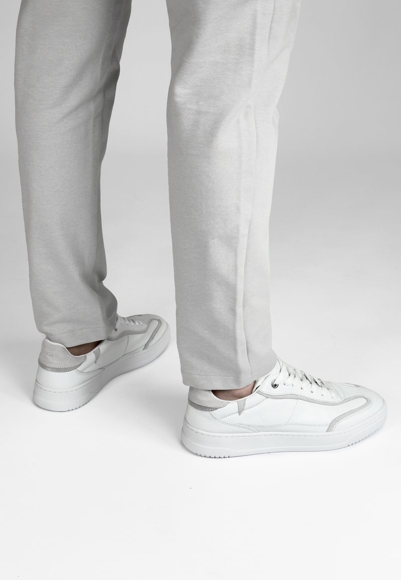 Witte leren sneakers met grijze accenten, ronde neus, vetersluiting en een gestructureerde zool, gecombineerd met lichtgrijze tapse broek.