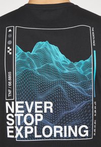 Svart T-shirt med en blå, intrikat designad bergsgrafik med rutmönster och texten "SLUTA ALDRIG UTFORSKA" i vitt.