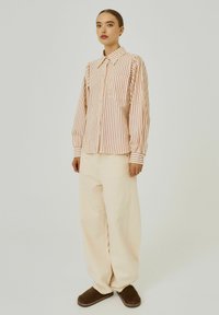 Gestreepte button-up blouse in crème en rood met een kraag, lange mouwen en een borstzak, gecombineerd met beige wijde pantalon en bruine schoenen.