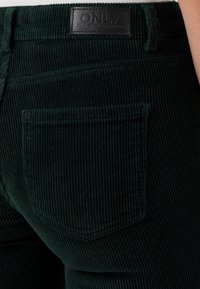 Tamnozelene baršunaste traperice s vertikalnom teksturom, s stražnjim džepom i crnom kožnom etiketom s utisnutim natpisom "ONLY".