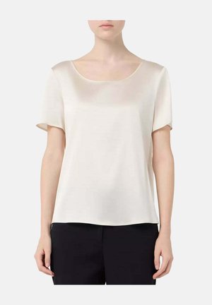 Femme portant un chemisier en satin ivoire à manches courtes avec un col rond, associé à un pantalon noir, montrée du cou aux hanches sur un fond uni.