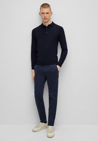 Marineblaues Langarm-Poloshirt mit Kragen, kombiniert mit marineblauen Chinos und weißen Sneakern, präsentiert an einem Modell vor einem neutralen Hintergrund.