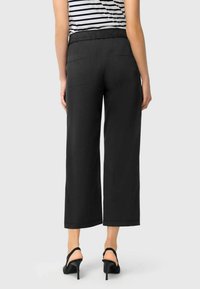 Black wide-leg pants with an elastic waistband, featuring two back pockets. Made from a smooth fabric, cropped above the ankle.