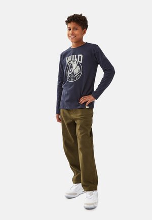 Marineblaues Langarm-T-Shirt mit Bärenmotiv, kombiniert mit olivgrünen Hosen und weißen Sneakers mit silbernen Akzenten. Einfaches, lässiges Outfit.