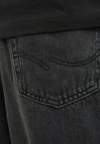 Jean en denim noir avec une poche arrière ornée de coutures discrètes et une finition texturée, montrant un gros plan du tissu.