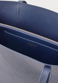 Tumši zils ādas somas iekšpuse ar rāvējslēdzēja kabatu, gludu tekstūru un zelta detaļām, iekšējā oderē ar zelta logotipu.