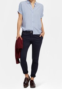 Jasnoniebieska, w paski koszula z krótkim rękawem, granatowe spodnie slim-fit, bordowy sweter zarzucony na ramię oraz brązowe mokasyny.