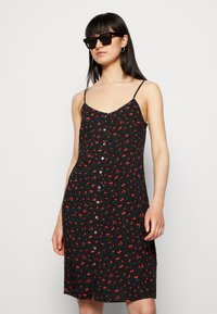 Vestido preto sem mangas com um padrão floral de cerejas vermelhas e folhas verdes, apresentando botões na frente e um corte descontraído.