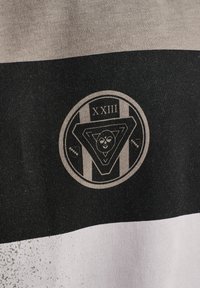 Sort, grå og hvide stribet stof med et cirkulært logo med et abstrakt ansigt og teksten "XXIII" centreret på den sorte del.