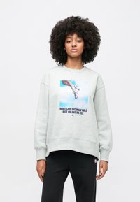 Γκρι φλις φούτερ με στρογγυλή λαιμόκοψη και πέδιλα στους ώμους. Διαθέτει γραφικό με χέρι και αθλητικά παπούτσια, με κείμενο από κάτω. Μαύρο παντελόνι.