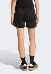 Pantaloncini sportivi neri con una consistenza liscia, vita elastica e una vestibilità comoda, abbinati a calzini neri e sneakers nere.