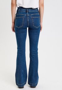 Ausgestellte blaue Jeans aus Denim mit hoher Taille, zwei Gesäßtaschen und einem Saum, der am Ende ausgestellt ist. Klassisches Fünf-Taschen-Design.