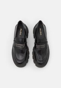 Mocassins en cuir verni noir avec des semelles en caoutchouc épaisses, présentant une finition lisse, un accent décoratif en argent et un design à bout rond.