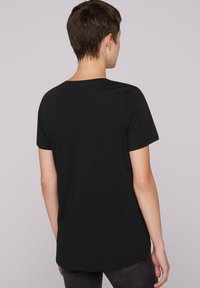 Camiseta negra de manga corta, con cuello redondo, corte regular, hecha de un tejido ligero. Textura suave sin patrones visibles.