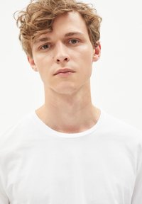 Witte ronde hals t-shirt gemaakt van katoen, met korte mouwen en een zachte textuur. Het model heeft tousled lichtbruin haar en een neutrale uitdrukking.