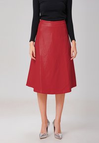 Jupe en cuir rouge en forme A avec une texture lisse, longueur mi-mollet et une taille ajustée, assortie à des escarpins argentés.