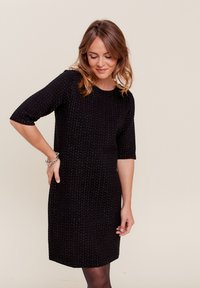 Robe noire à manches courtes, en tissu texturé avec un motif subtil. Encolure ronde, longueur genou, silhouette ajustée.