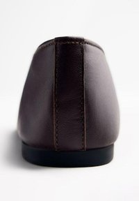 Zapato plano de cuero marrón con tacón redondeado, textura suave y costuras en contraste a lo largo de la costura trasera. Suela de goma negra.