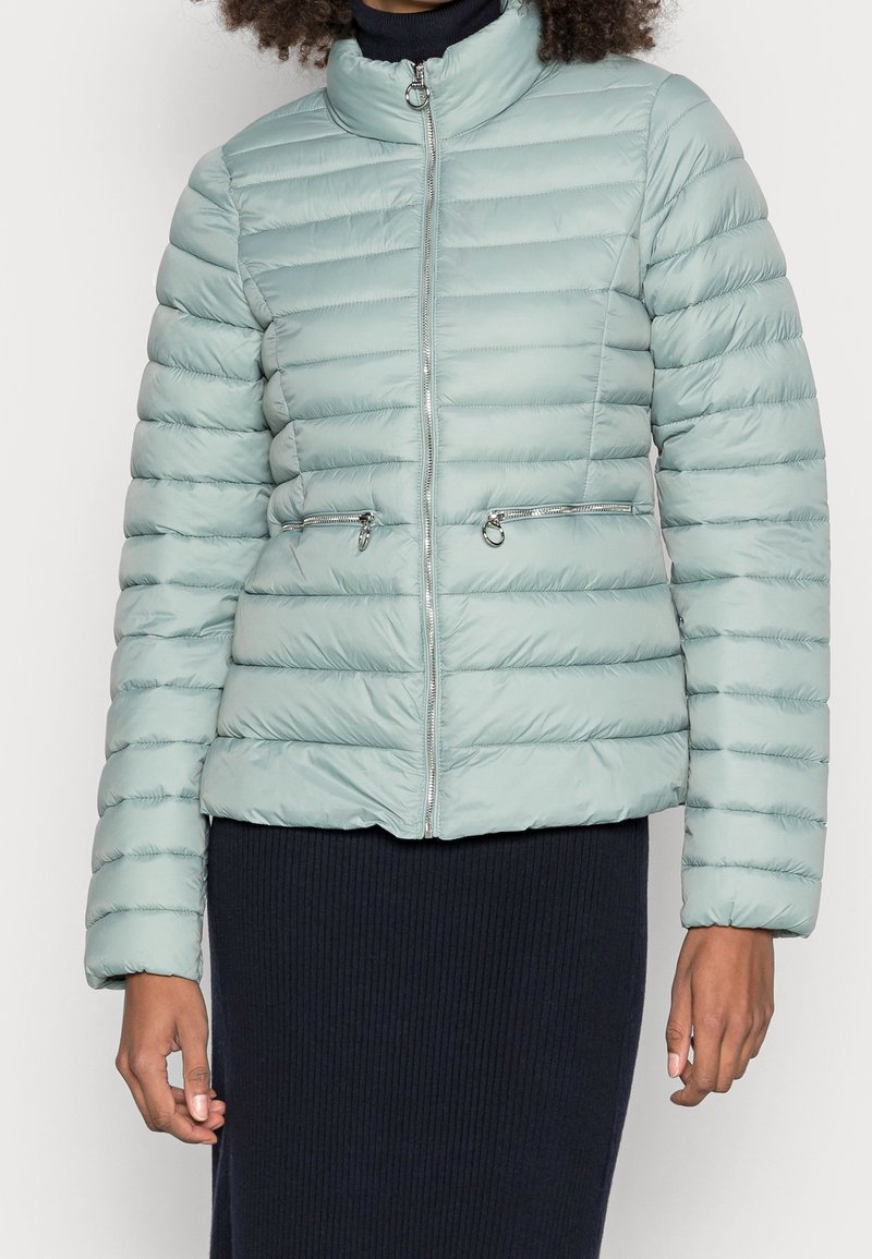 Doudoune vert clair avec matelassage horizontal, col montant et poches zippées. Présente des détails en argent et une coupe cintrée.