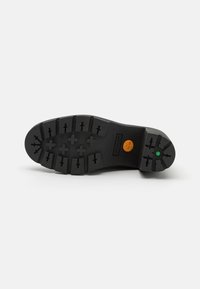 Black rubber sole with deep tread pattern, featuring Timberland logo and green accent. Textured surface for grip and durability.