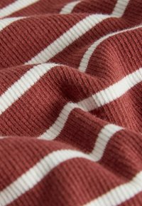 Rebrasta tkanina z izmenjujočimi se bordo in belimi črtami. Tekstura je mehka in rahlo puhasta, z vidno globino v gubah.
