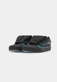 Zwarte sneakers met dikke veters, een ronde neus en teal accenten langs de zijkant. Voorzien van een textuurmateriaal en een stevige, lage profiel.