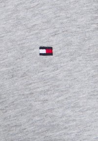 Grijze katoen stof met een subtiele textuur, voorzien van een kleine geborduurde patch in rood, wit en blauwe strepen.