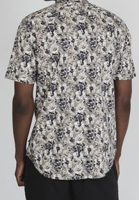 Koszula z krótkim rękawem z lekkiego materiału, w kwiatowy wzór w białym, granatowym i beżowym kolorze na jasnoszarym tle.