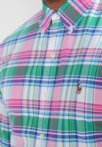 Flerfärgad rutmönstrad skjorta i nyanser av rosa, grönt och blått. Har knappkrage och broderad logotyp på bröstet. Bomullstyg.