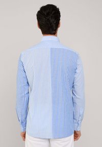 Camicia da uomo in blu e bianco a righe verticali. Presenta un colletto classico, maniche lunghe e polsini con bottone. Tessuto in cotone con una texture liscia.