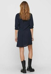 Námořnické šaty s puntíky, dlouhými rukávy a rozšířenou sukní, doplněné černými kotníkovými botami. Látka vypadá lehce a hladce.