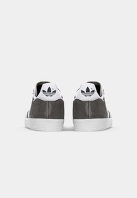Adidas lenkkarit harmaasta mokasta valmistetulla yläosalla, valkoisella kumipohjalla ja kolmella mustalla raidalla. Varustettu logolla kantapäässä ja pehmustetulla nilkkapaketilla.