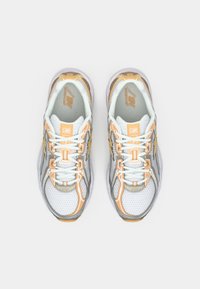 Par belih, oranžnih in sivih tekaških čevljev New Balance z mrežasto tkanino in vezalkami, pogled od zgoraj na beli podlagi.