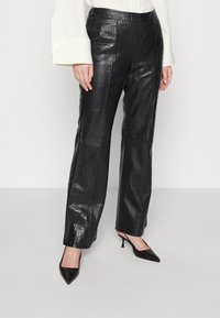 Zwarte nepleer broek met een krokodillenpatroon, voorzien van een rechte snit, hoge taille en een soepele textuur, gecombineerd met zwarte puntige schoenen.