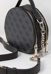 Borsa a spalla rotonda nera realizzata in materiale texturizzato. Presenta una chiusura con zip, hardware color oro e una tracolla a catena staccabile.
