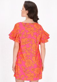 Rochie florală de un roz vibrant cu contururi portocalii. Prezintă mâneci volanate și o croială lejere. Materialul pare ușor și fluid.