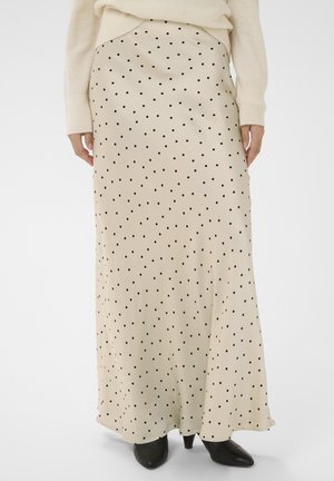 Jupe longue beige à pois noirs portée avec un pull crème et des bottines à talons pointues noires, vue de la taille aux pieds.