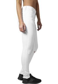 Vaqueros skinny blancos de mezclilla, con cintura alta y ligero desgastado en la rodilla, combinados con zapatillas deportivas negras.