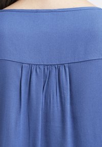 Blue fabric top featuring a pleated back design, smooth texture, and a wide neckline. Simple construction with no visible accents or patterns.