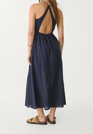 Marineblaues Maxikleid mit Rückenausschnitt und geraffter Taille. Hergestellt aus einem leichten Stoff. Kombiniert mit braunen Sandalen mit Schnallenakzenten.