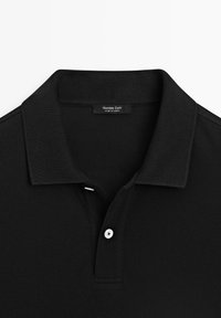 Polo noir avec un col plié et deux boutons, avec une étiquette Massimo Dutti à l'intérieur du col.
