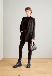 Must kollane ülerõivastus sobib kitsaste mustade teksade ja tume musta turtleneckiga, kaasas on suured mustad nahast kingad; käes on väike must käekott.