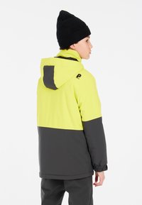 Veste jaune vif et gris foncé avec capuche, dotée de poignets élastiques et d'une coupe ajustée. Un bonnet en maille noir complète le look.
