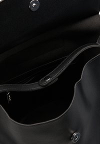 Intérieur d'un sac à main en cuir noir avec une texture lisse, une fermeture à pression et une poche latérale. Design minimaliste, spacieux à l'intérieur.