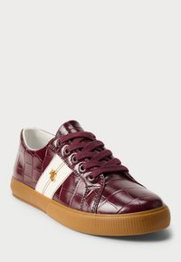 Μπορντό συνθετικά αθλητικά παπούτσια με υφή κροκόδειλου, λεπτομέρειες λευκής ρίγας, χρυσό λογότυπο και καφέ λάστιχο. Κλείσιμο με κορδόνια και στρογγυλή μύτη.