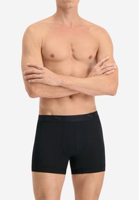 Schwarze Boxerbriefs aus glattem Material mit einer engen Passform. Sie haben einen kontrastierenden elastischen Bund mit dem Markennamen "PUMA" in Schwarz.