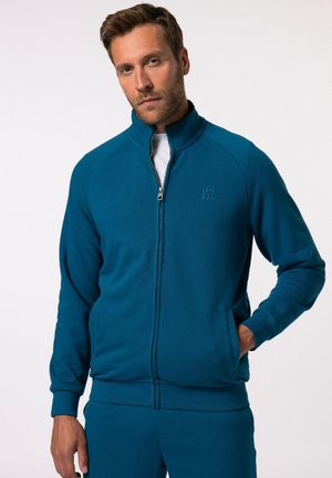 Giacca zip-up color teal realizzata in tessuto morbido, con colletto alto, polsini a costine e tasche frontali. Presenta un logo discreto sul petto.
