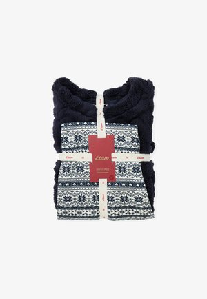 Wrap in peluche blu navy con motivo di fiocchi di neve bianchi e bordi decorativi; include nastri con marchio e un'etichetta in rosso e bianco.